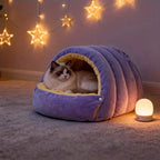 Purple cat cave bed with a cat resting inside beside a small lamp